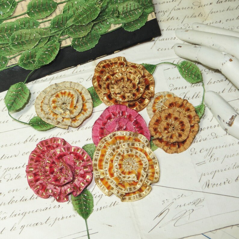May include: Six vintage fabric flowers in various colors and patterns. The flowers are made of velvet and have a layered, ruffled design. The flowers are arranged on a piece of paper with handwritten text.