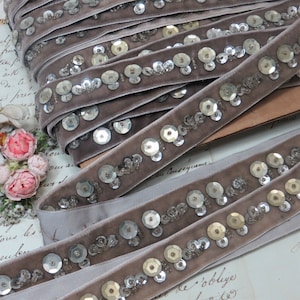 May include: A close-up of a gray velvet ribbon with silver and gold sequins. The ribbon is folded in multiple layers, showing the detail of the sequins.
