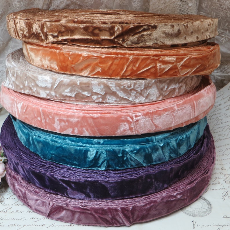May include: A selection of velvet ribbon rolls in a range of colours. The colours include shades of brown, peach, pink, teal, and purple. The ribbon has a soft, textured appearance, and is likely used for crafting or decorative purposes.