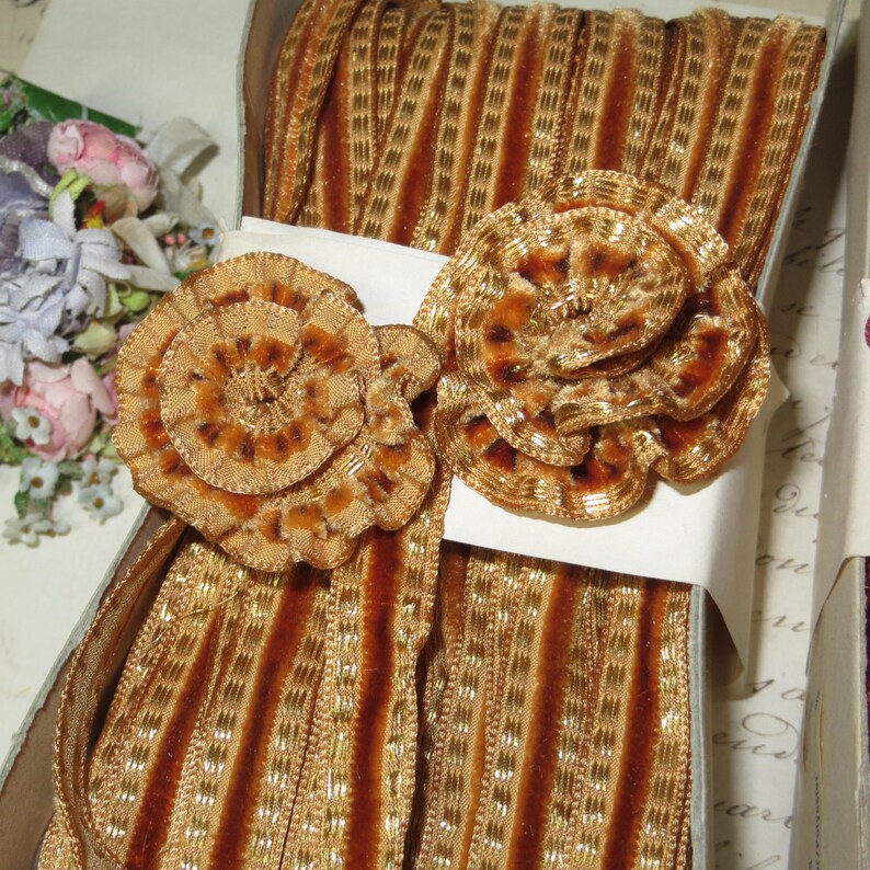 May include: A spool of brown and gold striped ribbon with two decorative velvet rosettes. The ribbon is trimmed with gold thread.
