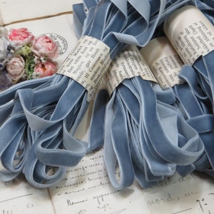 May include: A pile of light blue velvet ribbon spools. The ribbon is wrapped around itself and tied with a white tag. The tag has text in a foreign language.