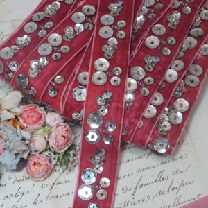 May include: Pink velvet ribbon trim with silver sequins. The ribbon is folded and stacked, showing the sequins from different angles.