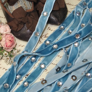 May include: Blue velvet ribbon with silver rhinestones. The ribbon is folded and twisted, showing the rhinestones on both sides.