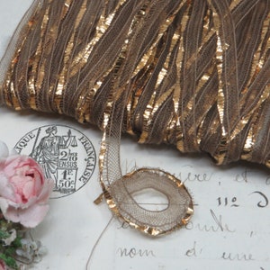 May include: A spool of brown and gold metallic trim. The trim is made of a thin, woven fabric with a gold metallic thread running through it. The trim is coiled and ready to be used for crafting or decorating.