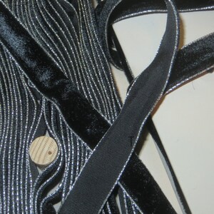 May include: Black velvet ribbon with a silver metallic trim. The ribbon is folded and stacked, showing the detail of the trim.