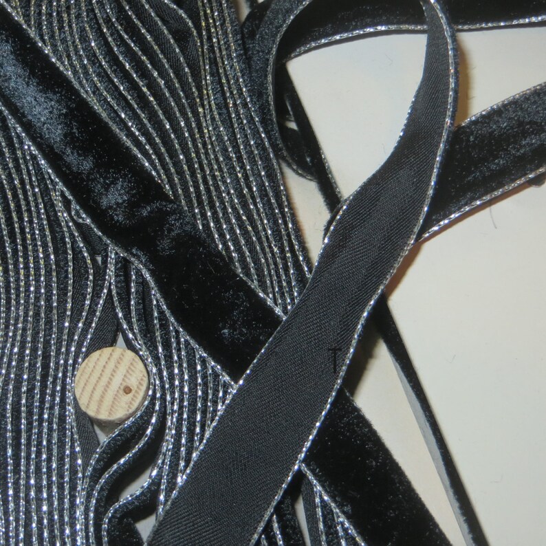 May include: Black velvet ribbon with a silver metallic trim. The ribbon is folded and stacked, showing the detail of the trim.