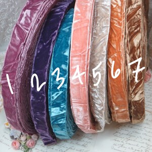 May include: A collection of velvet ribbon in a spectrum of colours, from deep purple to teal, peach, and gold. The ribbon is rolled, displaying its soft texture and sheen. The image showcases the variety of colours suitable for crafting or decorative use.