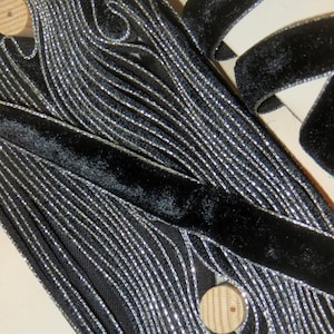 May include: Black velvet ribbon with silver metallic trim. The ribbon is folded and layered, showing the texture of the fabric.