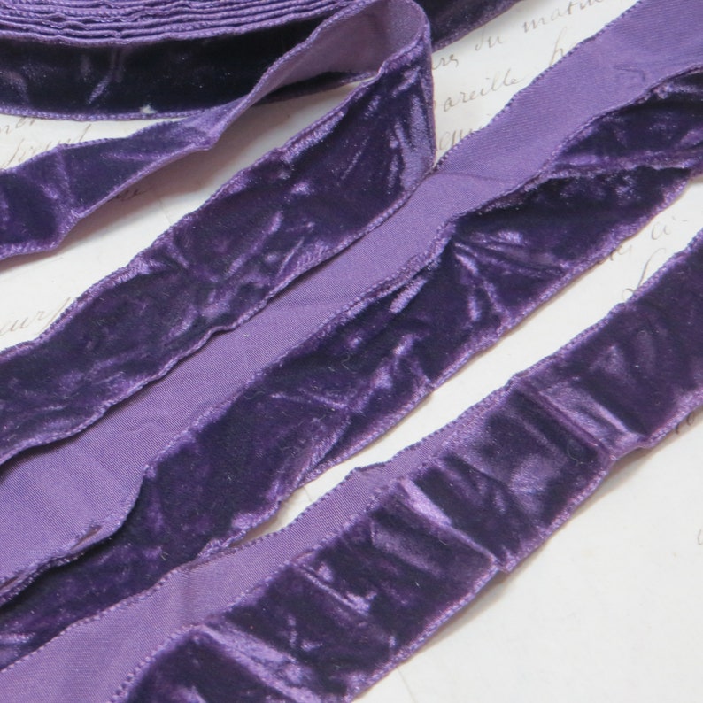 May include: Close-up of a roll of deep purple velvet ribbon. The ribbon has a soft, textured appearance with a lighter purple fabric on the edges. The ribbon is likely used for crafting, sewing, or decorative purposes.