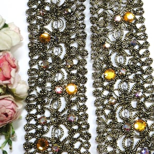 May include: Gold beaded trim with iridescent and gold-toned rhinestones. The trim has a delicate floral pattern.