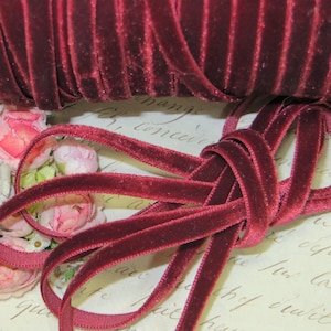 May include: A spool of burgundy velvet ribbon. The ribbon is approximately 1/4 inch wide and is shown in a loose coil.