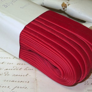 May include: A roll of vibrant red velvet ribbon, partially unwound from its white cardboard packaging. The ribbon is tightly wound, revealing a smooth, luxurious texture. The packaging has text that reads "33 yds" and "Scarlet".