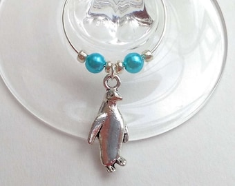 May include: A silver penguin charm hangs from a wine glass charm. The charm is attached to a silver wire ring with turquoise beads.