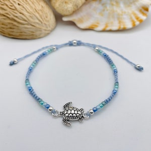 May include: A blue and green beaded bracelet with a silver turtle charm. The bracelet is adjustable and can be worn on the wrist or ankle.