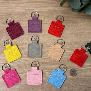 May include: A selection of leather keyrings in shades of burgundy, purple, red, yellow, grey, beige, pink, and blue. Each keyring features a rectangular design with a silver key ring.
