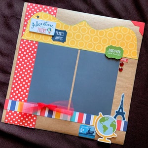 May include: A scrapbook page with a brown background and a yellow, white, and red polka dot border. The page has two black photo frames with a red ribbon and a red bow. The page also has a green sticker that says "Discover New Places" and a red sticker that says "Pack".