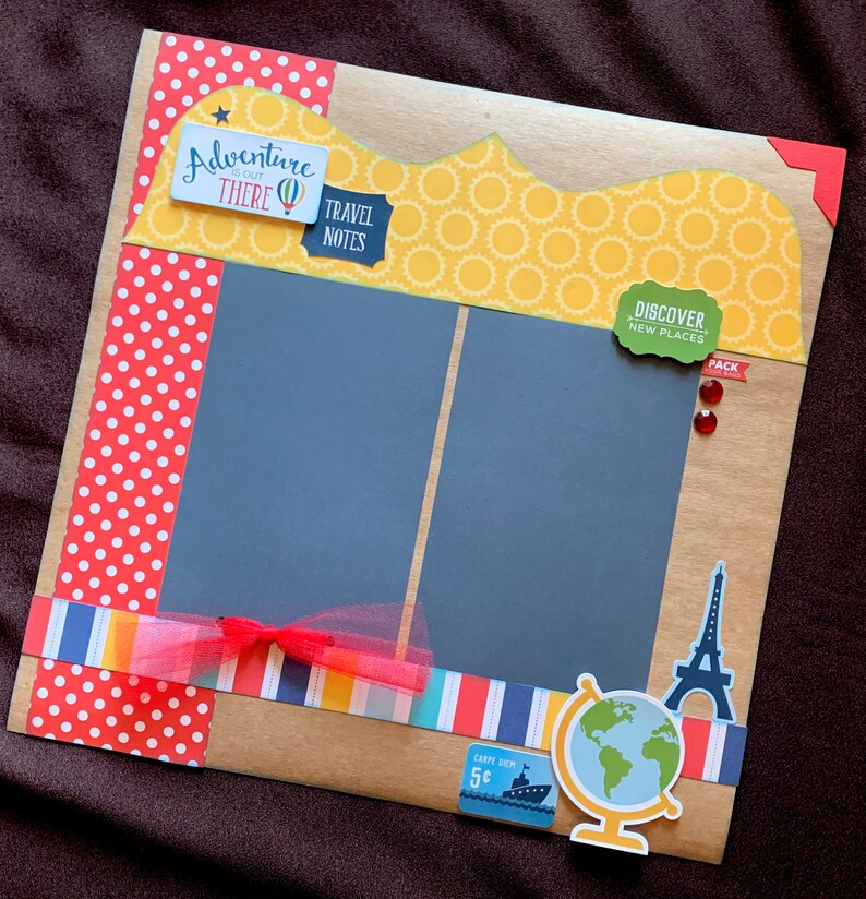 May include: A scrapbook page with a brown background and a yellow, white, and red polka dot border. The page has two black photo frames with a red ribbon and a red bow. The page also has a green sticker that says "Discover New Places" and a red sticker that says "Pack".