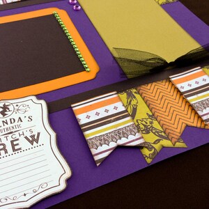 May include: Purple scrapbook page with black, orange, and yellow patterned paper flags. The flags have a witch theme and say "Glenda's Authentic Witch's Brew".