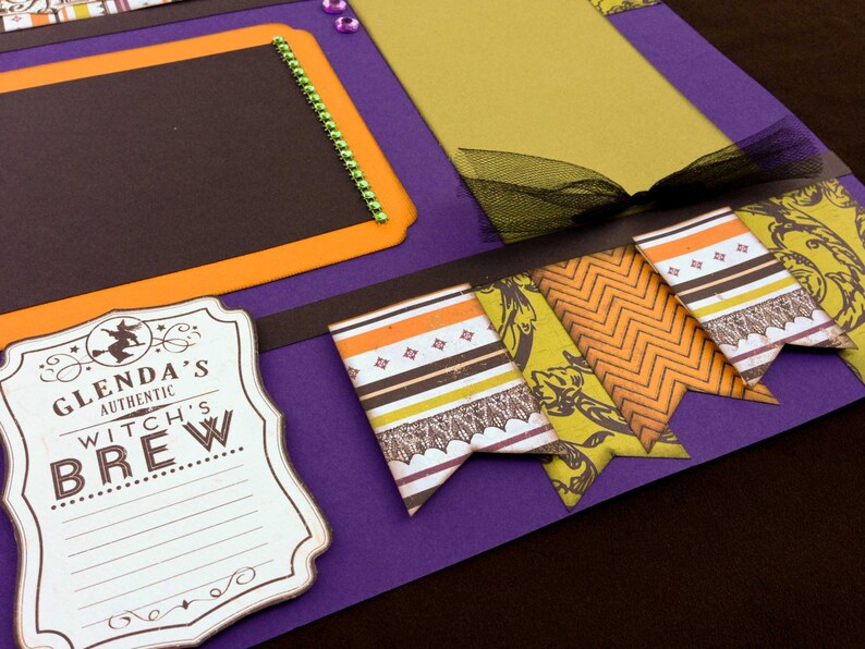 May include: Purple scrapbook page with black, orange, and yellow patterned paper flags. The flags have a witch theme and say "Glenda's Authentic Witch's Brew".