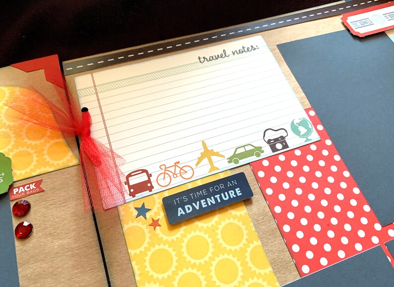 May include: A scrapbook page with a travel theme. The page has a lined section for writing travel notes, a red polka dot patterned paper, a yellow paper with a sunburst pattern, and a black paper with the text "It's time for an adventure".
