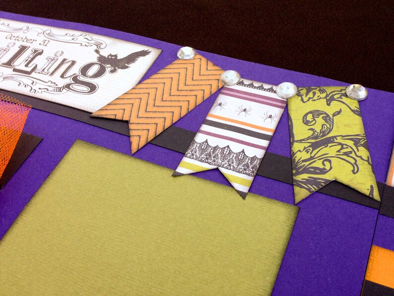 May include: Purple scrapbook page with a green, orange, and black patterned paper background. The page has a black and white banner with the text "October 31st, " "Tricking" and "Treating" written on it. There are three decorative paper flags with a black, white, and orange pattern.
