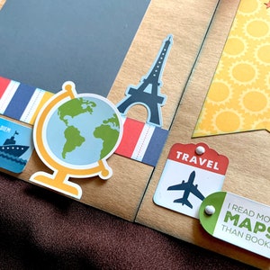 May include: A scrapbook page with a travel theme. The page features a globe, a silhouette of the Eiffel Tower, a travel tag with an airplane, and a tag that says "I read more maps than books".