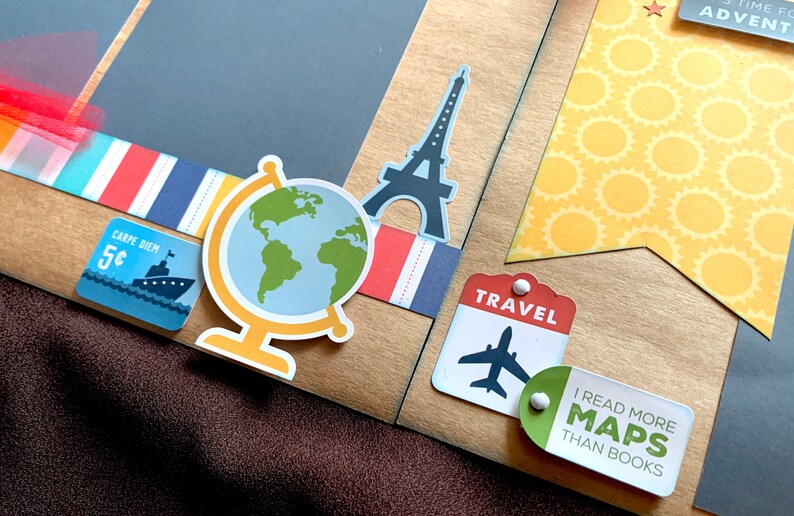 May include: A scrapbook page with a travel theme. The page features a globe, a silhouette of the Eiffel Tower, a travel tag with an airplane, and a tag that says "I read more maps than books".