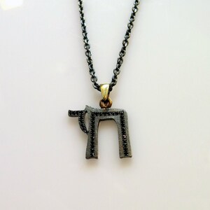May include: A silver chain necklace with a black Hebrew letter pendant. The pendant is encrusted with small black stones.