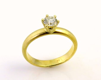 May include: A gold engagement ring with a single, round-cut diamond. The ring features a classic six-prong setting and a smooth, brushed gold band. The diamond sparkles brightly against the warm gold.