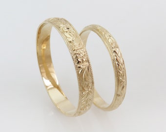 May include: Two gold wedding bands with intricate floral designs.