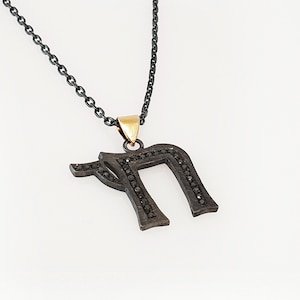 May include: A black chain necklace with a black metal pendant in the shape of the Hebrew letter 'nun' with black diamonds. The pendant has a gold bail.