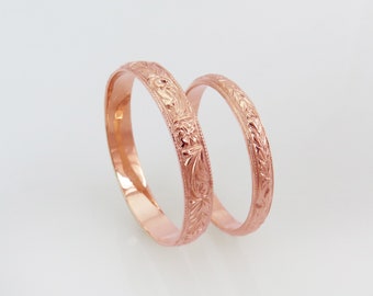 May include: Two rose gold wedding bands with intricate floral engravings.