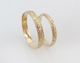May include: Two gold wedding bands with intricate floral designs.