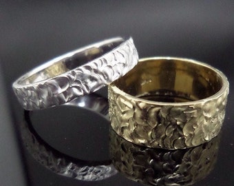 May include: Two wedding bands, one silver and one gold, with a textured, hammered finish.