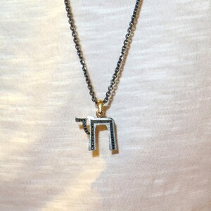May include: A silver chain necklace with a pendant featuring the Hebrew letter 'Chai' in black.