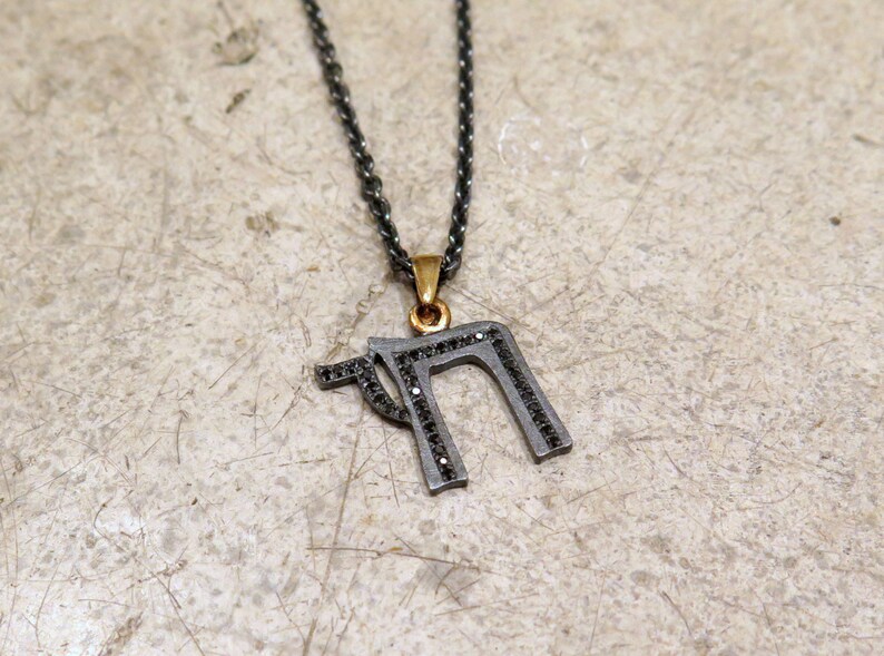 May include: A silver chain necklace with a pendant shaped like the Hebrew letter 'Heh' set with black diamonds. The pendant is accented with a gold bail.