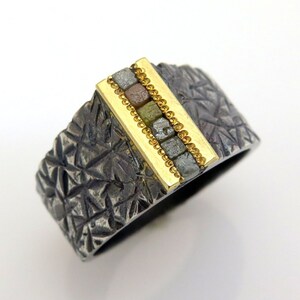 May include: A silver ring with a textured surface and a gold band set with a row of small, colorful diamonds.