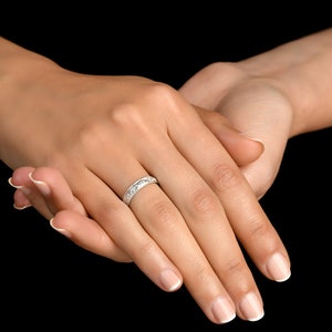 May include: A silver-toned band ring featuring a repeating engraved pattern along its outer surface. The ring has a polished metallic finish and a consistent width, encircling the finger with a detailed, textured design that catches the light.