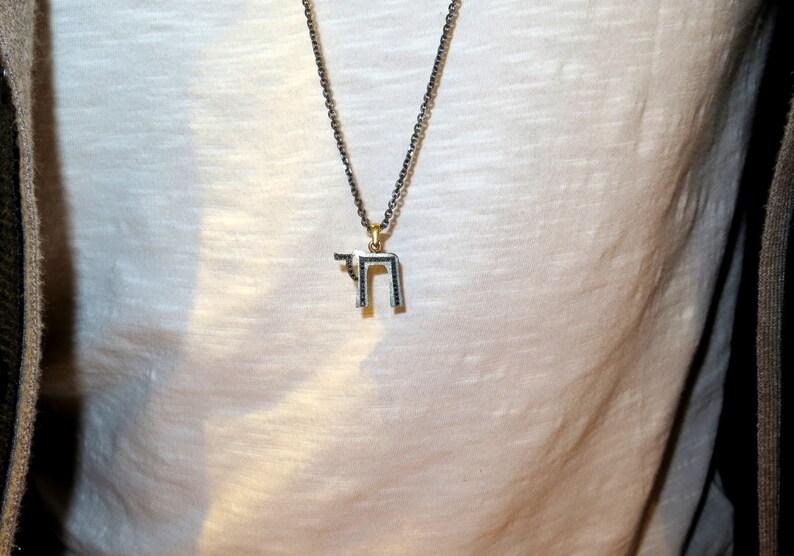 May include: A silver chain necklace with a pendant featuring the Hebrew letter 'Chai' in black.