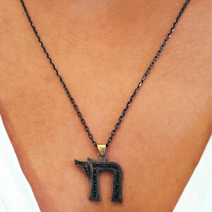 May include: A black chain necklace with a black pendant shaped like the Hebrew letter 'Chai' with black diamonds.