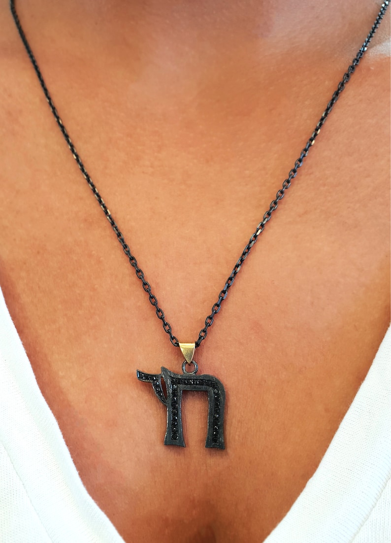 May include: A black chain necklace with a black pendant shaped like the Hebrew letter 'Chai' with black diamonds.