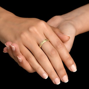 May include: A yellow gold band ring featuring a delicate, repeating engraved floral pattern across its entire outer surface. The ring has a polished finish and a slim, rounded profile, showcasing intricate botanical details etched into the metal.