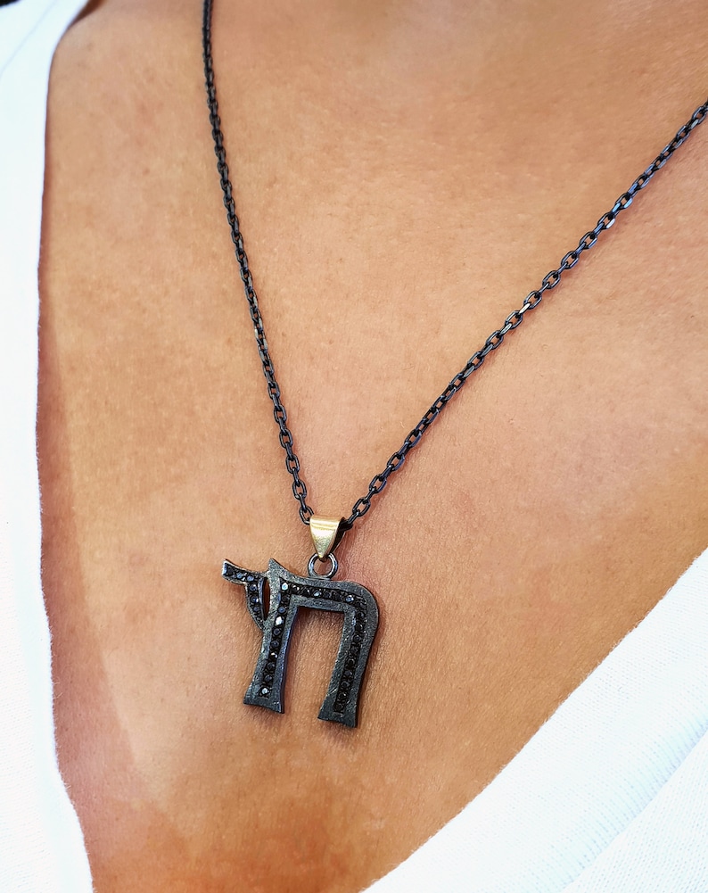 May include: A black chain necklace with a pendant shaped like the Hebrew letter 'Chai' set with black stones.