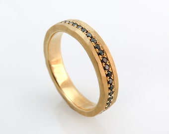 May include: A gold band ring with a row of black diamonds set into the metal.
