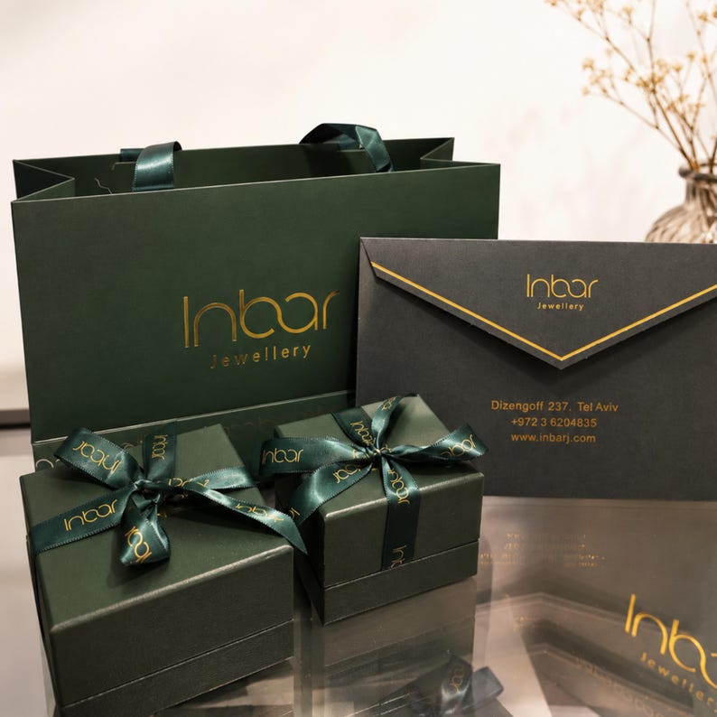May include: A dark green shopping bag, two dark green square gift boxes tied with matching branded ribbons, and a dark grey envelope. Each item features the gold Inbar Jewellery logo. The envelope includes the address Dizengoff 237, Tel Aviv.