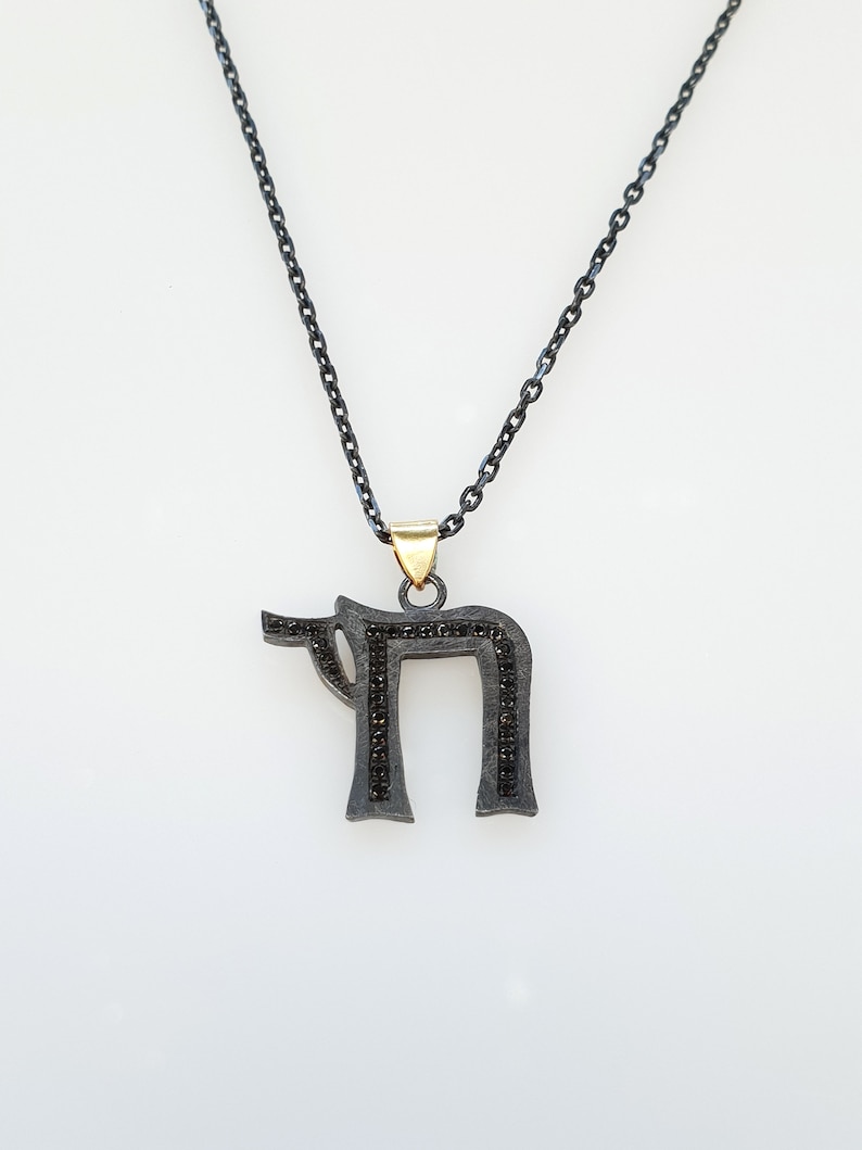 May include: A black chain necklace with a silver pendant in the shape of the Hebrew letter 'Chai' with black diamonds.