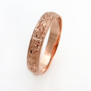 May include: A rose gold ring featuring an intricate engraved pattern of leaves and small flowers along the outer band. The edges of the ring are detailed with a fine beaded texture, and the interior surface has a smooth, polished finish.