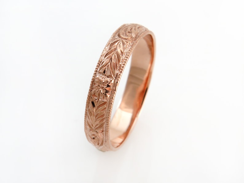 May include: A rose gold ring featuring an intricate engraved pattern of leaves and small flowers along the outer band. The edges of the ring are detailed with a fine beaded texture, and the interior surface has a smooth, polished finish.