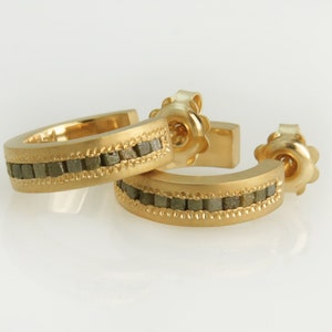 May include: A pair of gold hoop earrings with a row of small, gray stones set in the band.