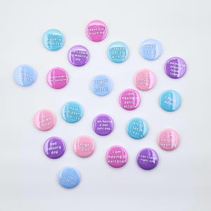 Pastel pinback buttons with text: I need space, I am having a bad pain day, I have mobility Issues, low energy day, please don't touch me, don't touch my mobility aid, please speak clearly, I can't speak right now, I am non-verbal, I have mobility issues, I am having sensory issues today, bad sensory day, I am hard of hearing, I might faint, please be patient with me, awkward but friendly, I can't speak right now, I am neurodivergent, situationally non-speaking, I am having a meltdown